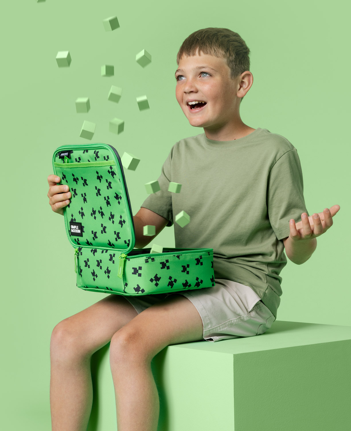 Boy sitting with green lunchbox, cubes floating around.