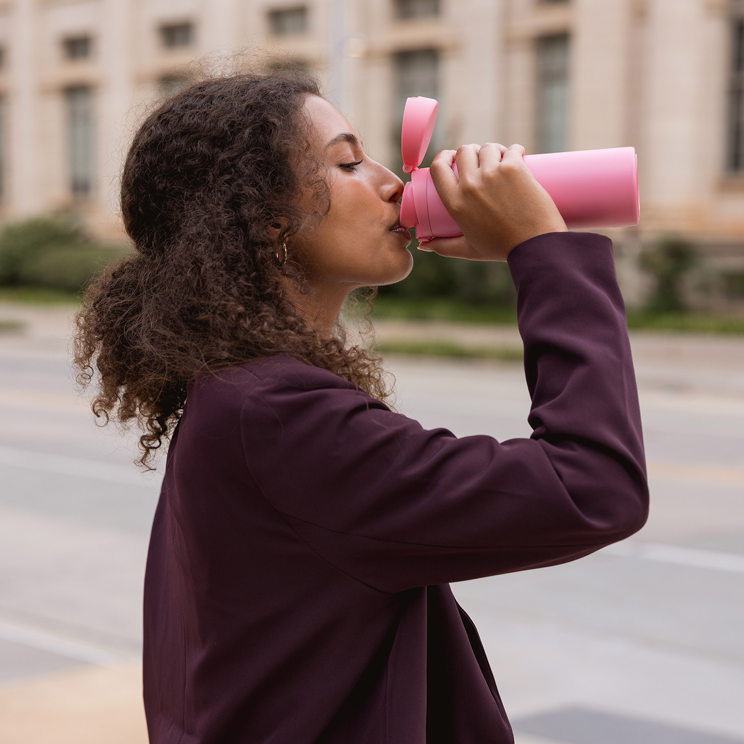 Person drinking from a pink bottle outdoors.