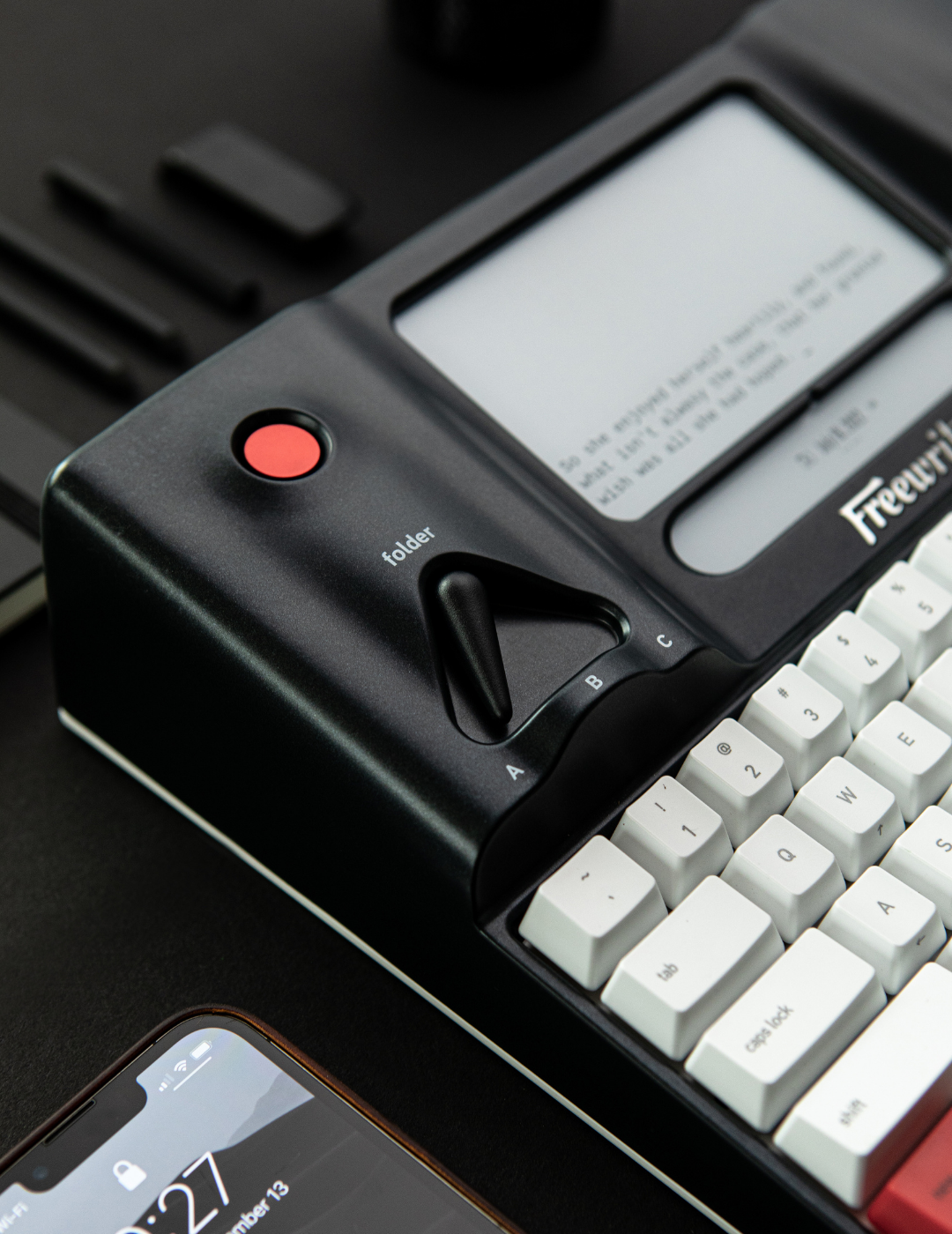 Close-up of a retro-style typewriter keyboard and screen with nearby smartphone.