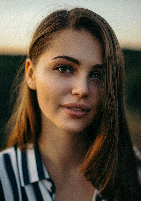 Woman with long hair in a striped shirt, outdoors with blurred background.