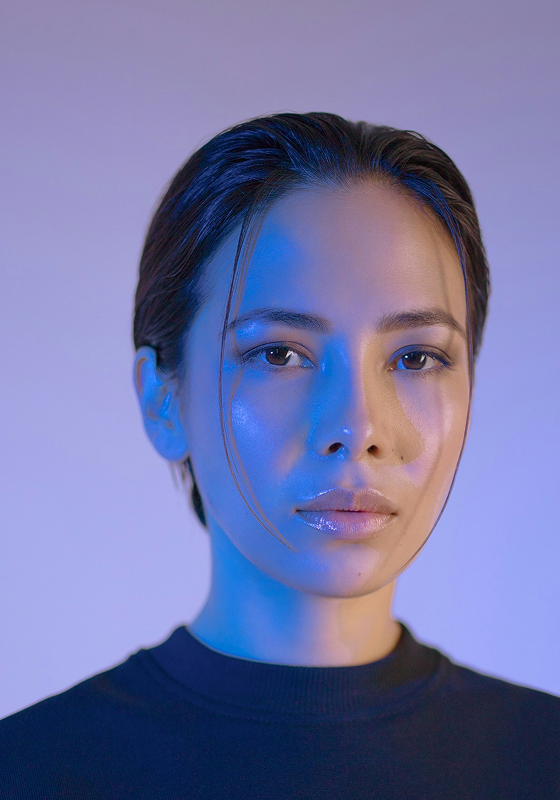 Person with blue and natural lighting on face, neutral expression.
