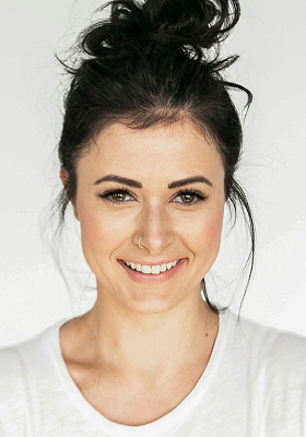 Person with dark hair in a bun, wearing a white shirt, smiling.