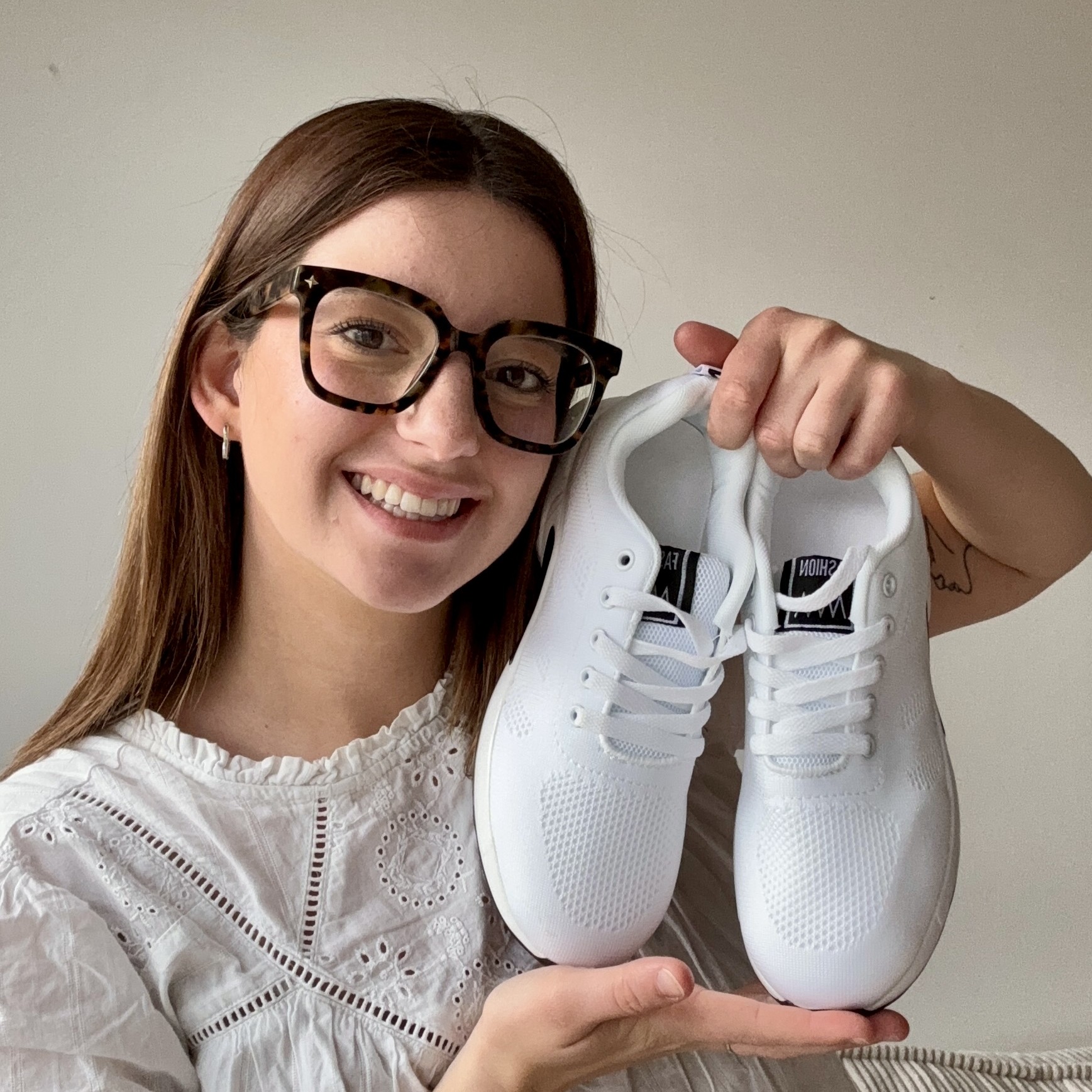 Person smiling and holding a pair of white sneakers.