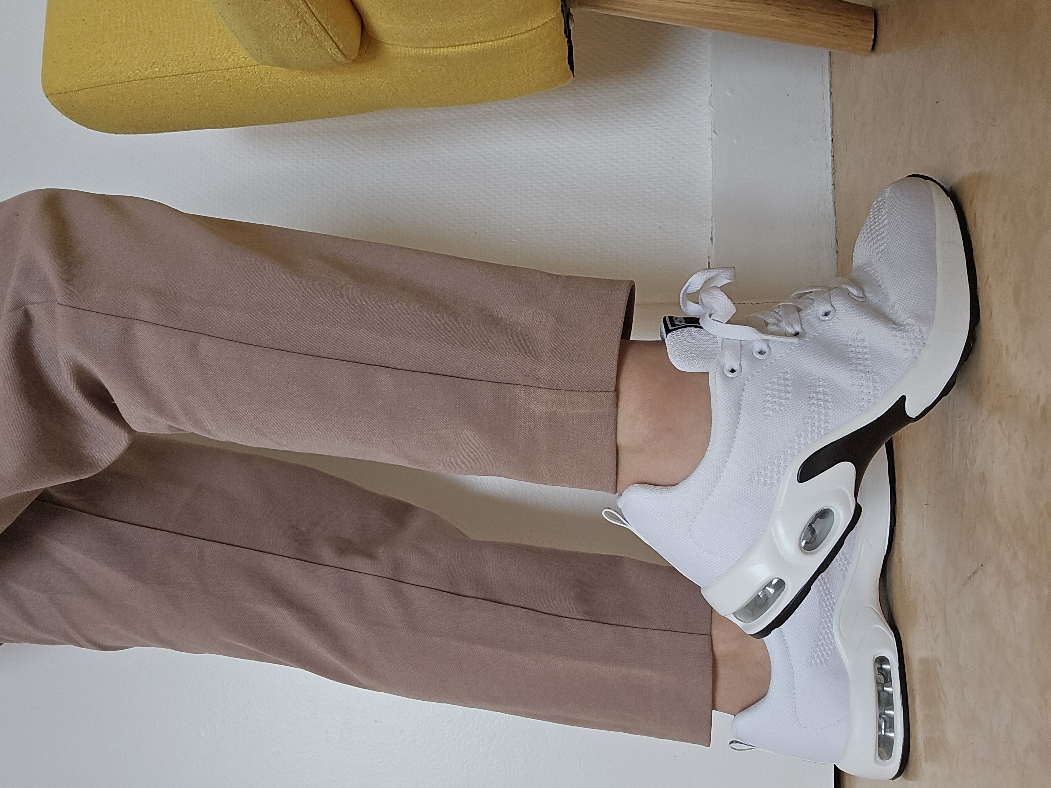 Person wearing white sneakers and beige pants near a yellow chair.