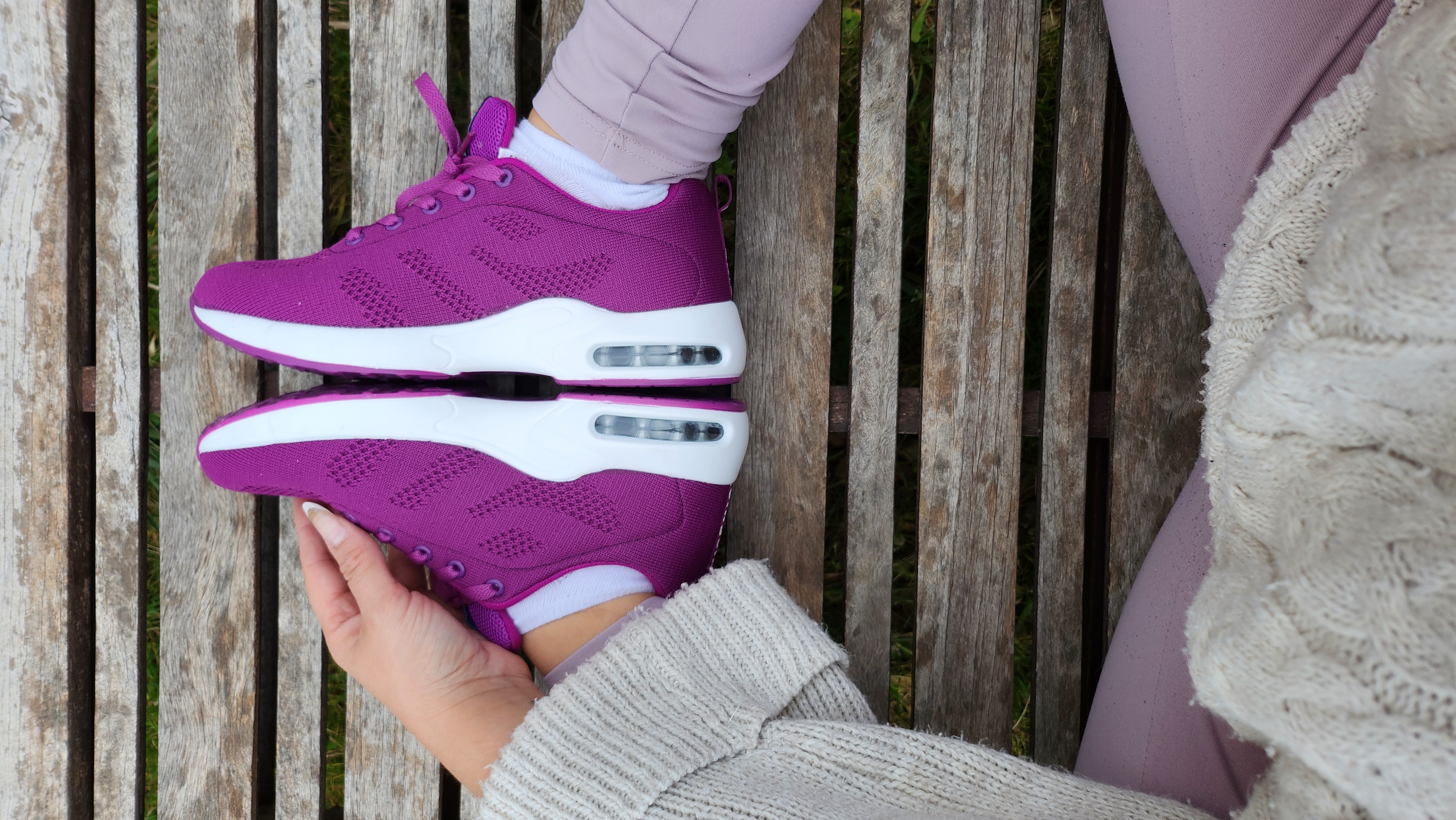 Person holding purple sneakers on a wooden bench.