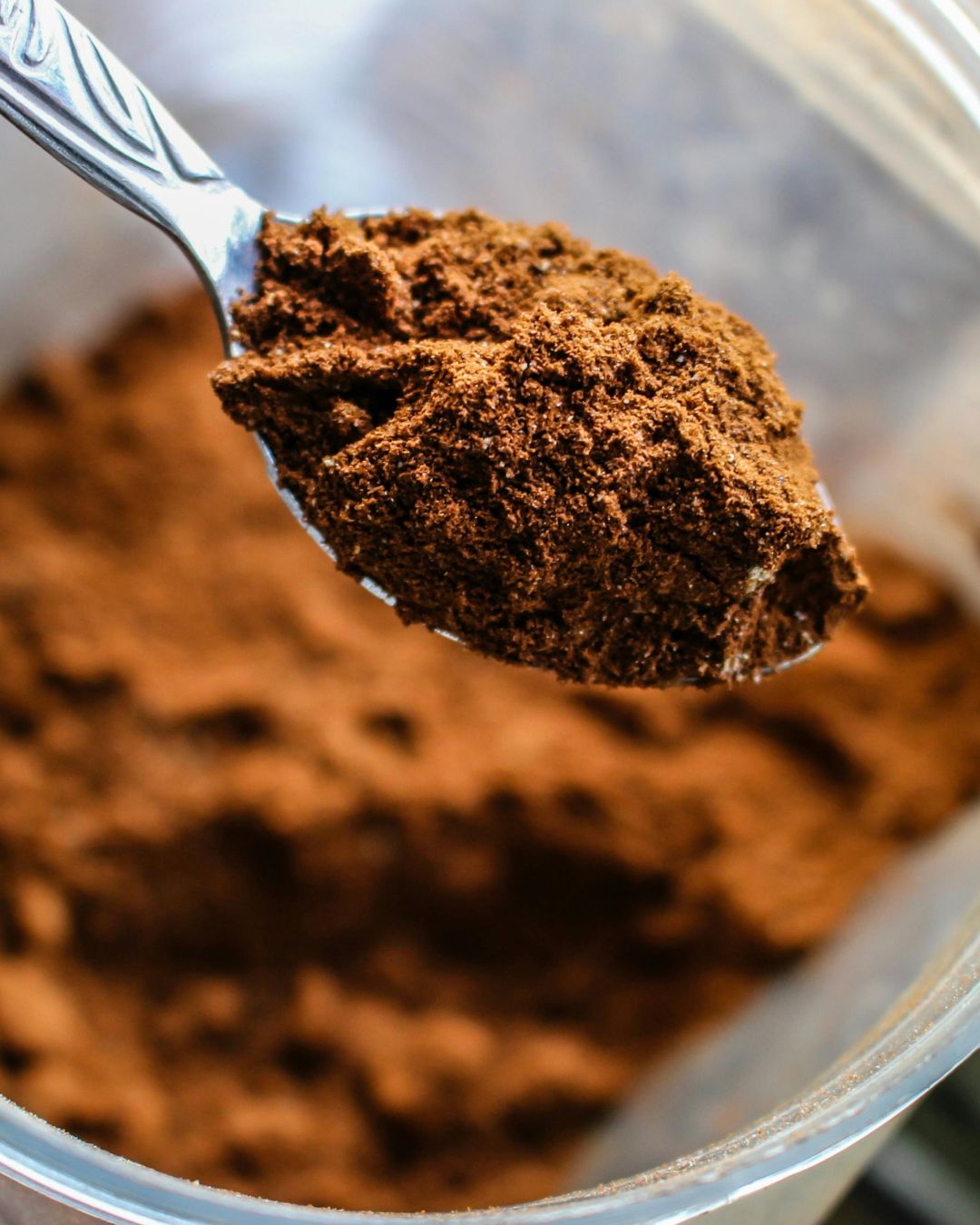 Close-up of a spoonful of ground coffee over a container.