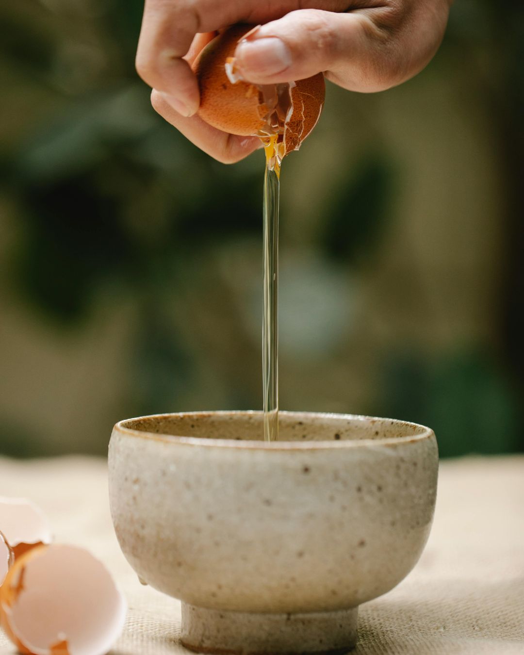 Hand cracking an egg into a ceramic bowl.