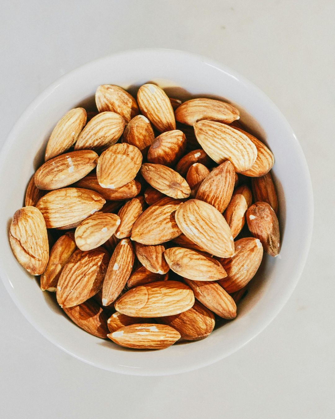 A white bowl filled with whole almonds on a light surface.