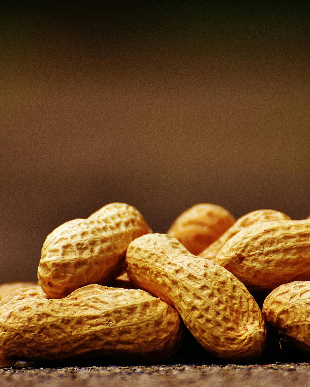 A pile of unshelled peanuts on a surface.
