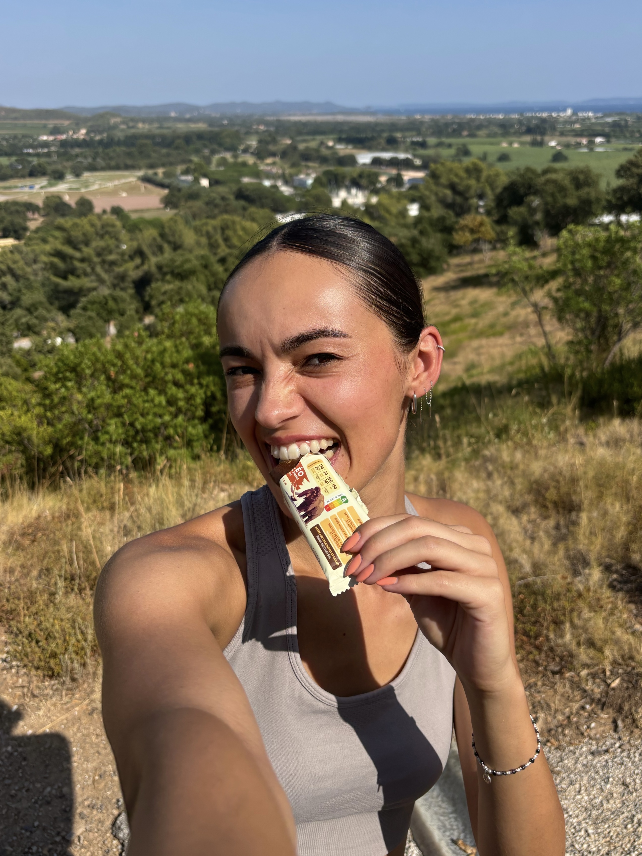 Person taking a selfie while eating a snack bar outdoors.