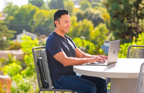 Man sitting outdoors using a laptop at a round table.