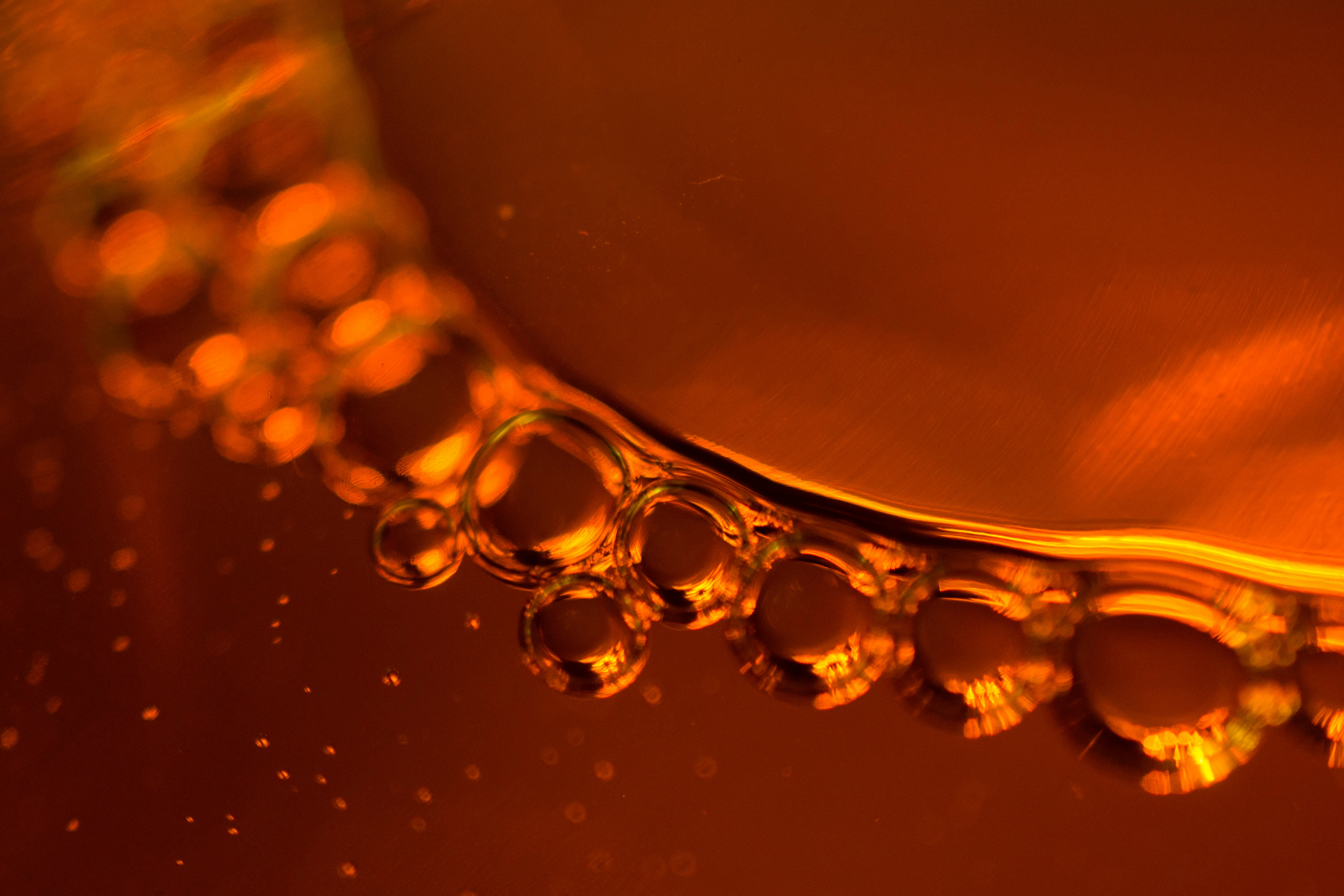A macro photograph of bubbles forming on the surface of an amber-colored liquid.