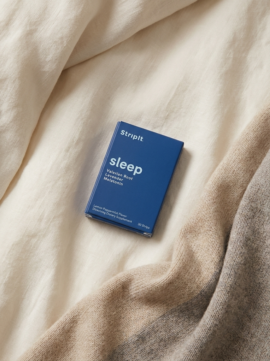 A blue box of StripIt sleep supplement lying on a soft, rumpled bed with a knit blanket.