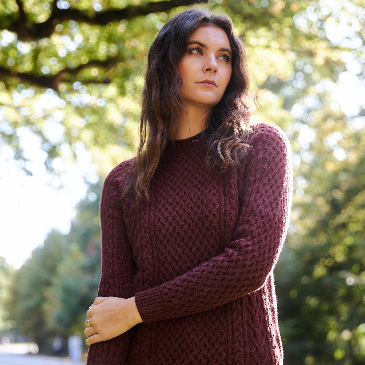 Woman in a maroon sweater standing outdoors with trees in the background.