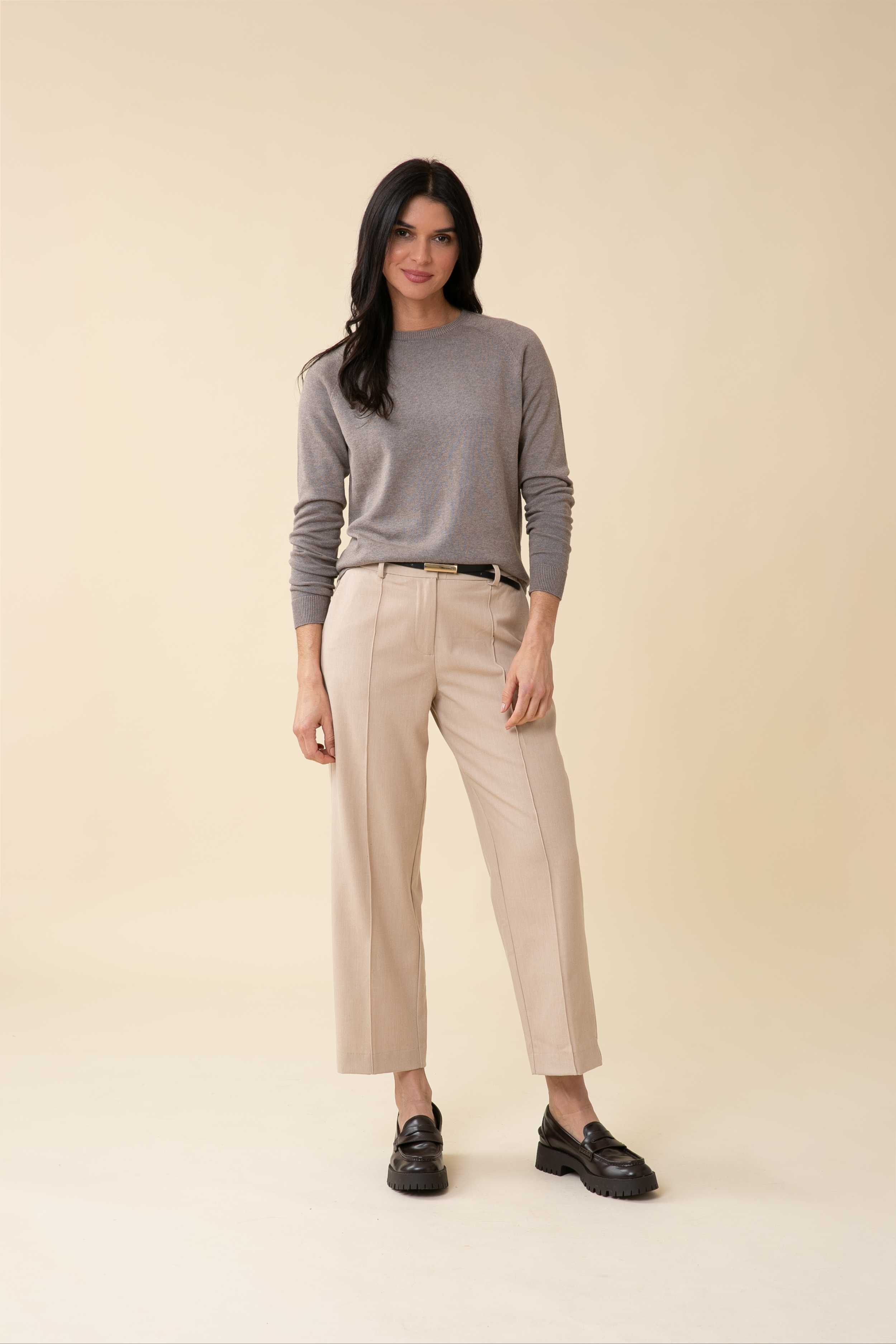 A woman with long dark hair models a grey sweater, beige trousers, and black loafers.