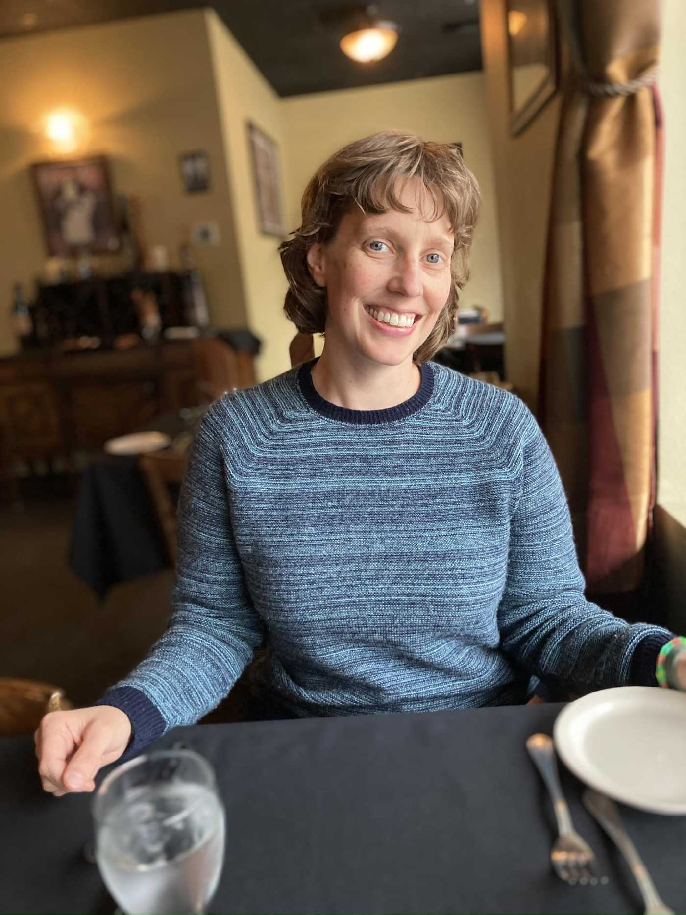 Customer MK M. sitting indoors wearing a blue heathered Oliver Charles sweater, demonstrating the comfort and versatility of the product.