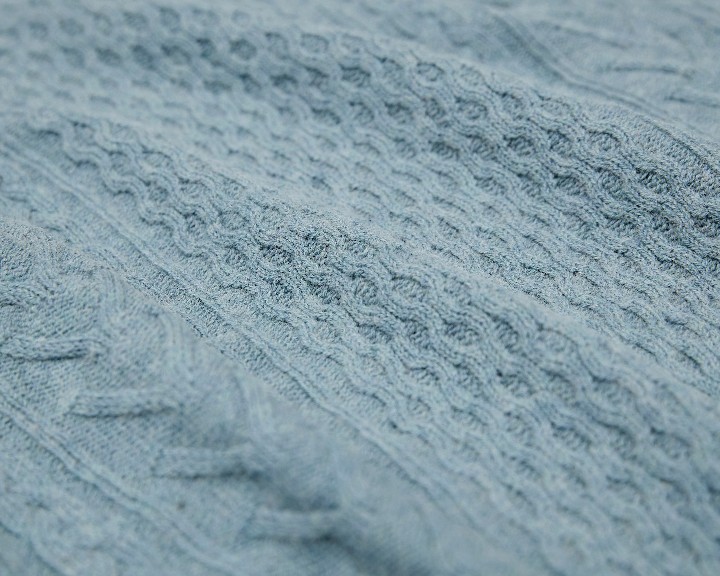 Close-up of a blue knitted fabric with a cable pattern.