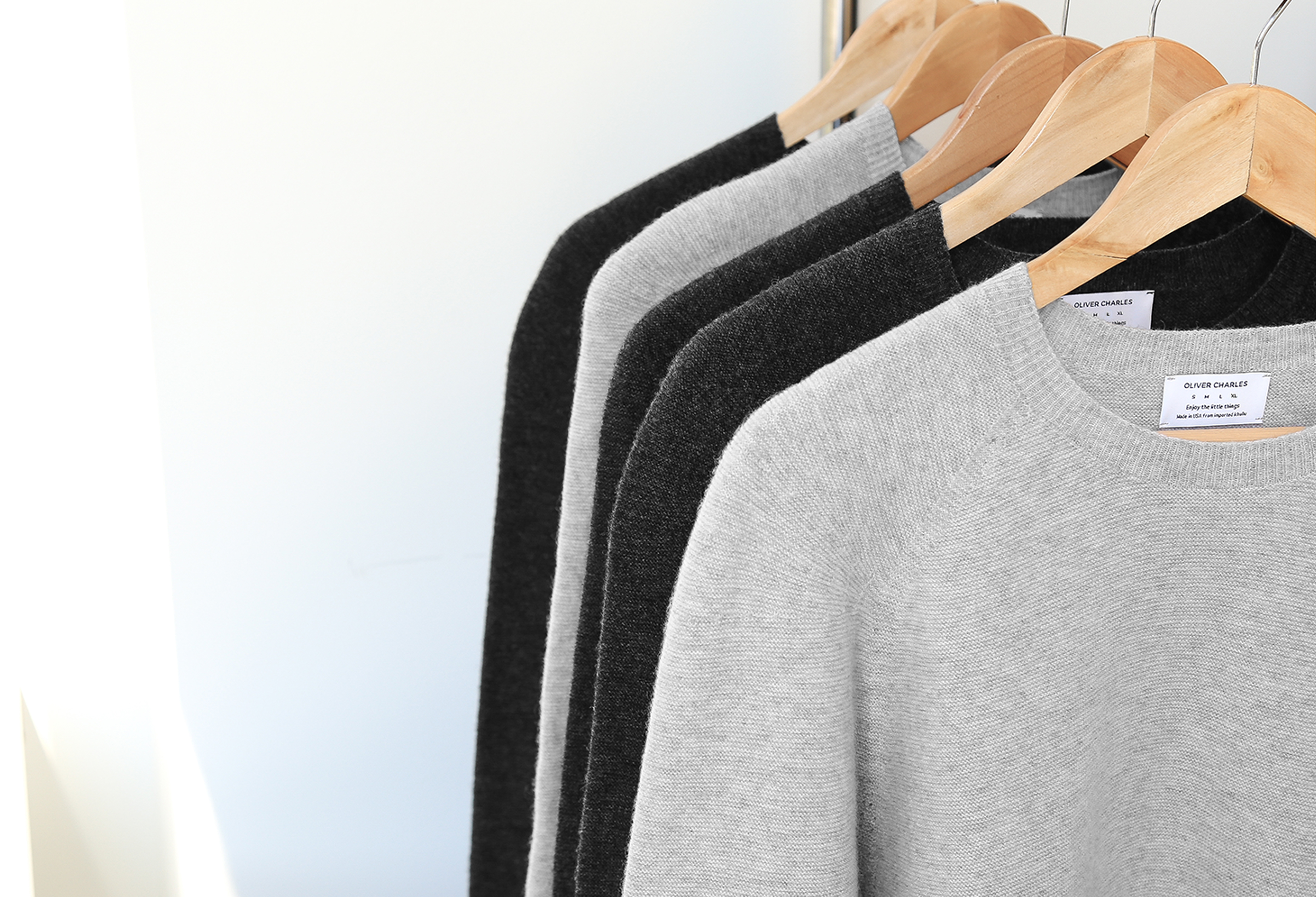 Four sweaters in gray and black on wooden hangers. 