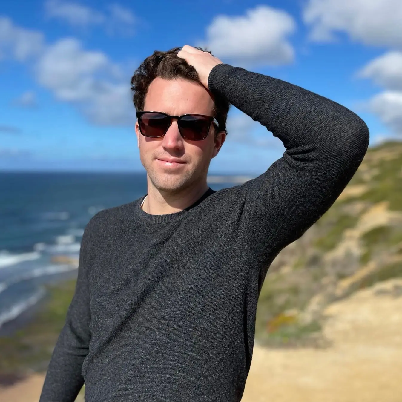 Person in sunglasses standing by a coastal landscape. 