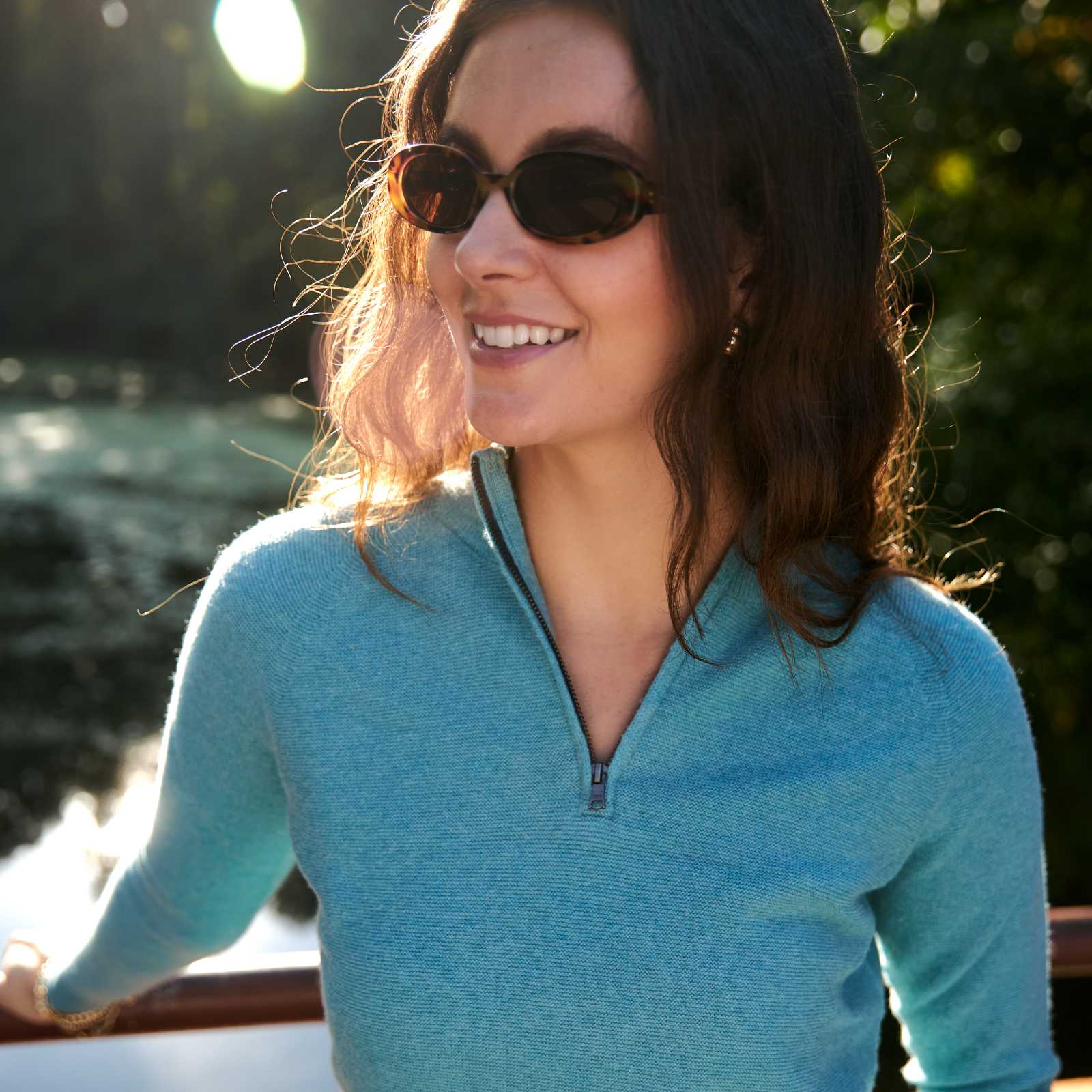 Woman in sunglasses and blue sweater smiling outdoors.
