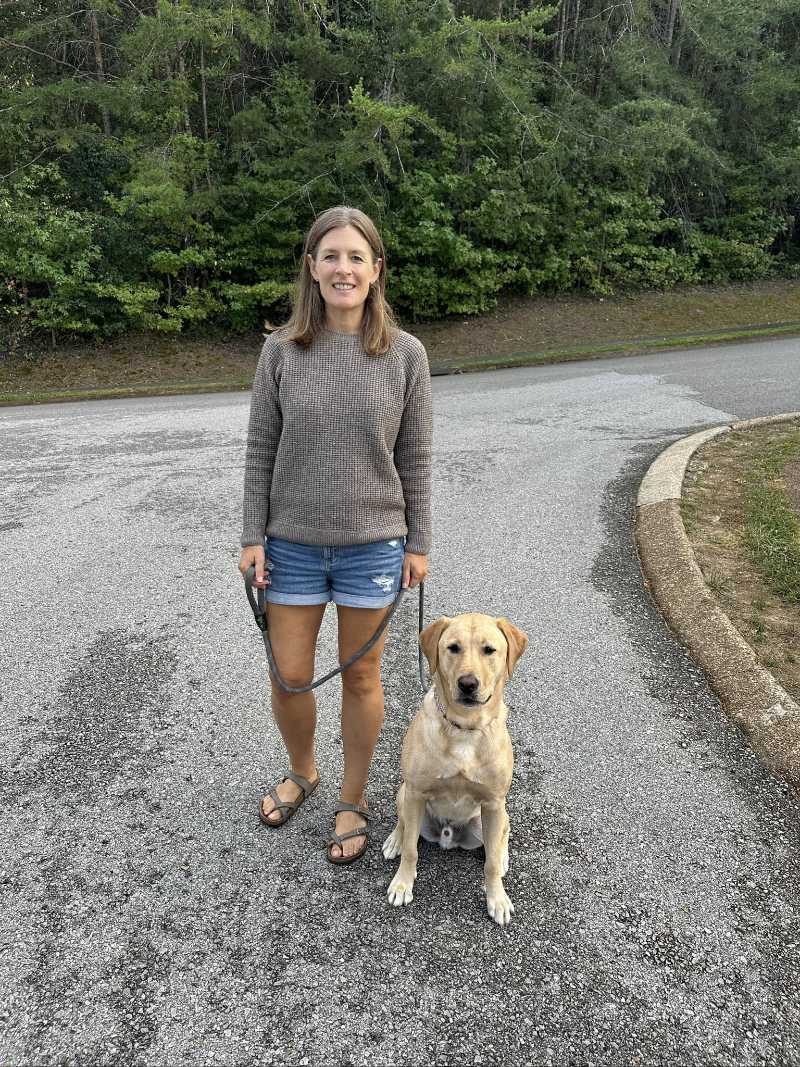 Customer Kristi L. walking with her golden retriever dog on a gravel path while wearing an Oliver Charles sweater.