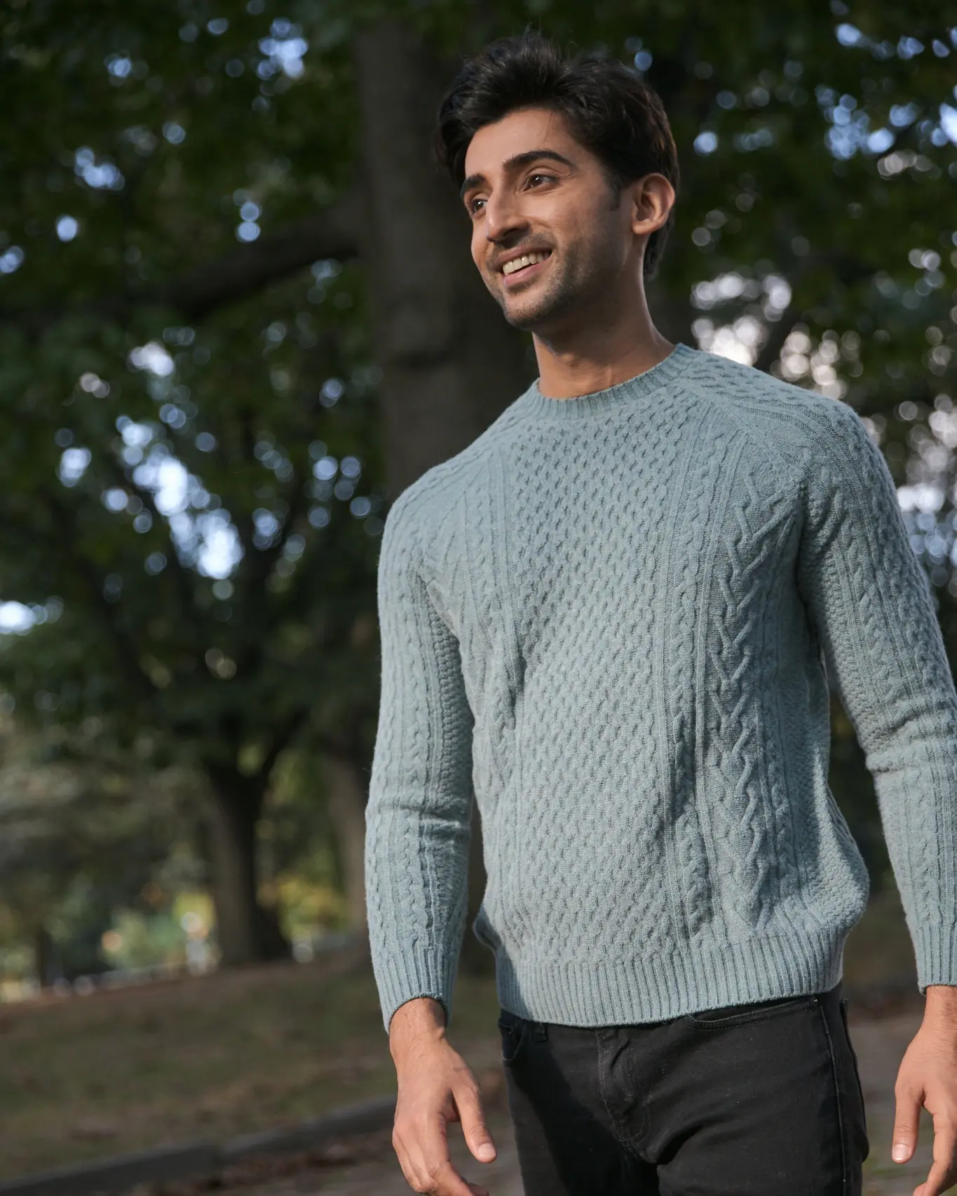 Person in a light blue sweater smiling outdoors with trees in the background. 