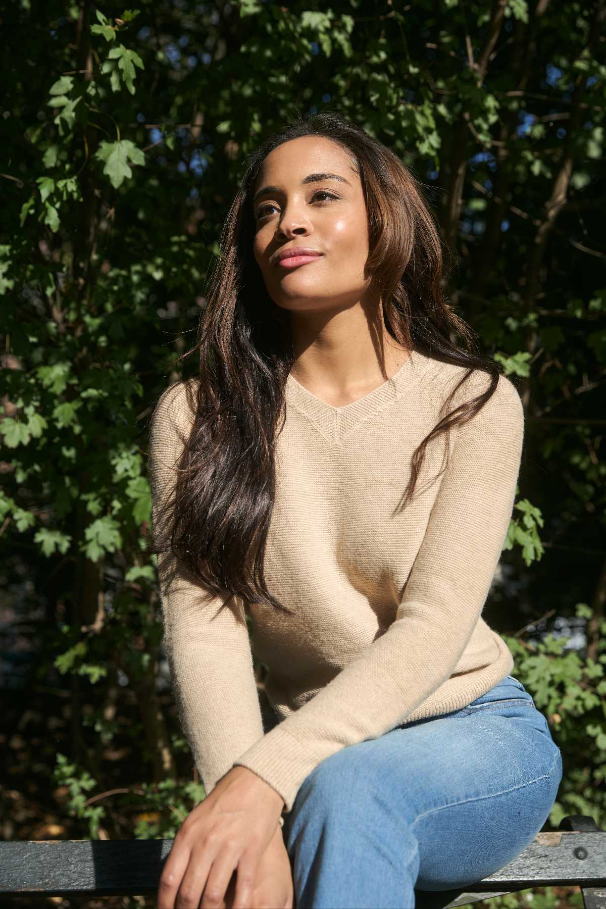 Person sitting on a bench in sunlight, surrounded by green leaves.