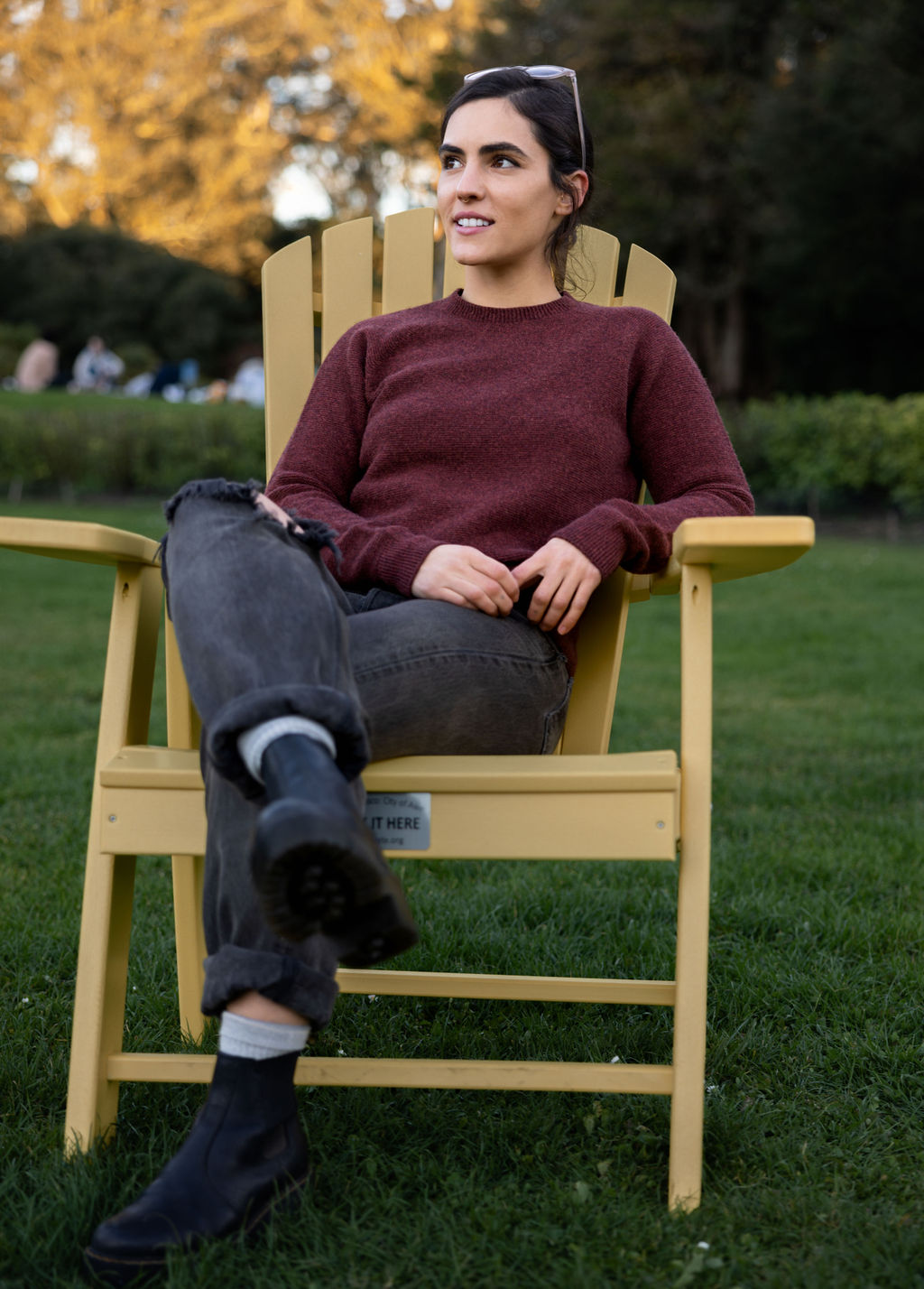 Person sitting on a yellow chair in a park, wearing a maroon sweater. 
