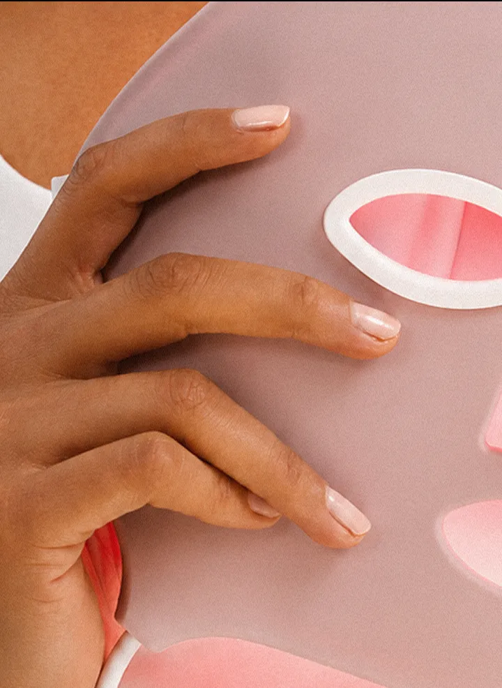 A close-up of a hand with a nude manicure holding a pink, reusable sheet mask.