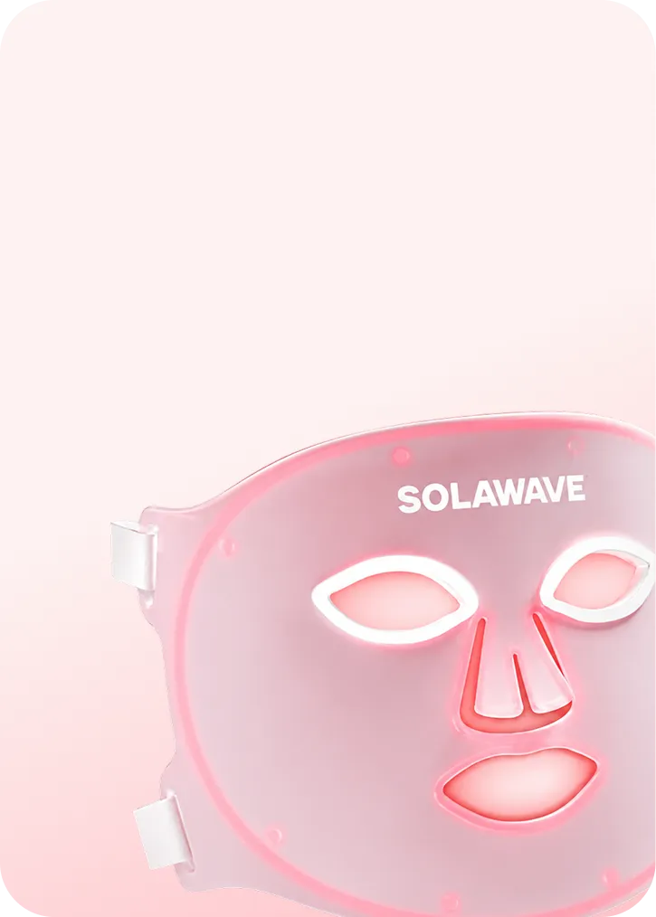 A close-up of the pink Solawave LED light therapy face mask glowing against a light pink background.