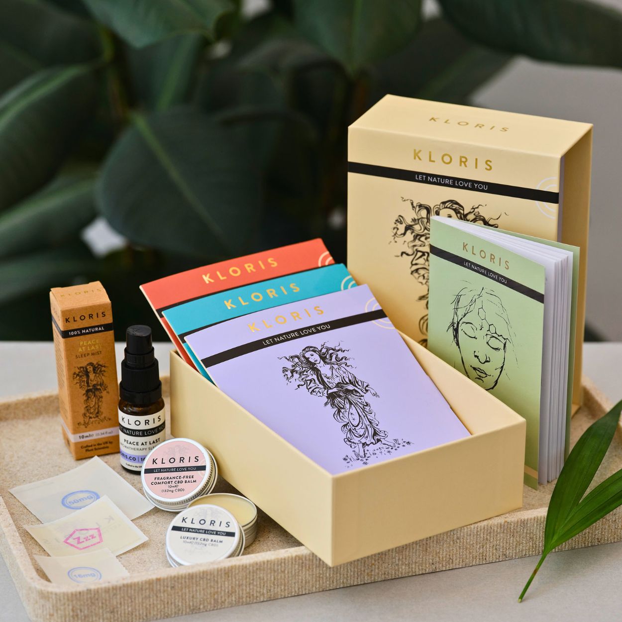 A gift set of KLORIS brand wellness products including balms and mists arranged on a beige tray.