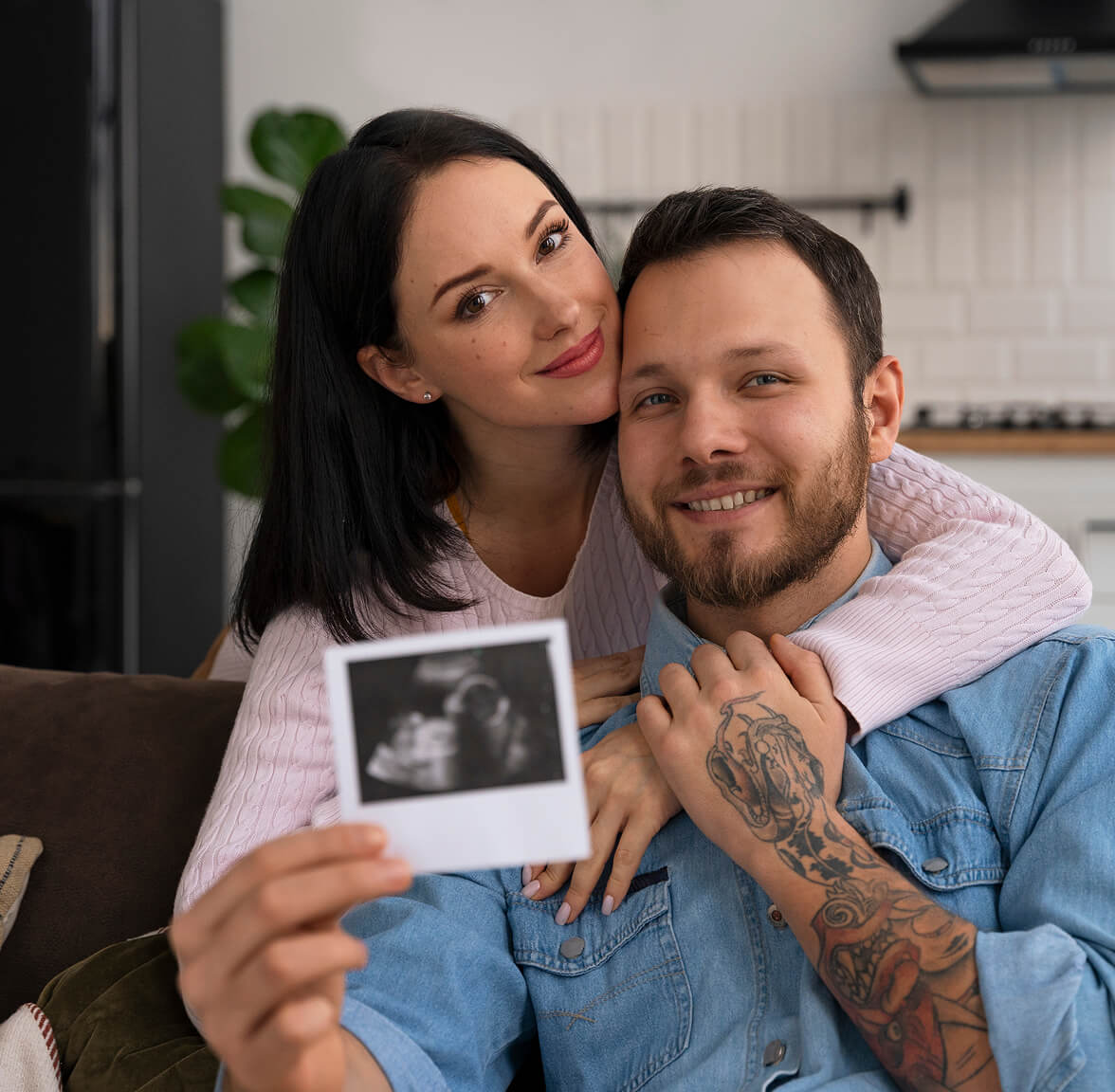 Couple smiling and holding an ultrasound photo in a cozy home setting.