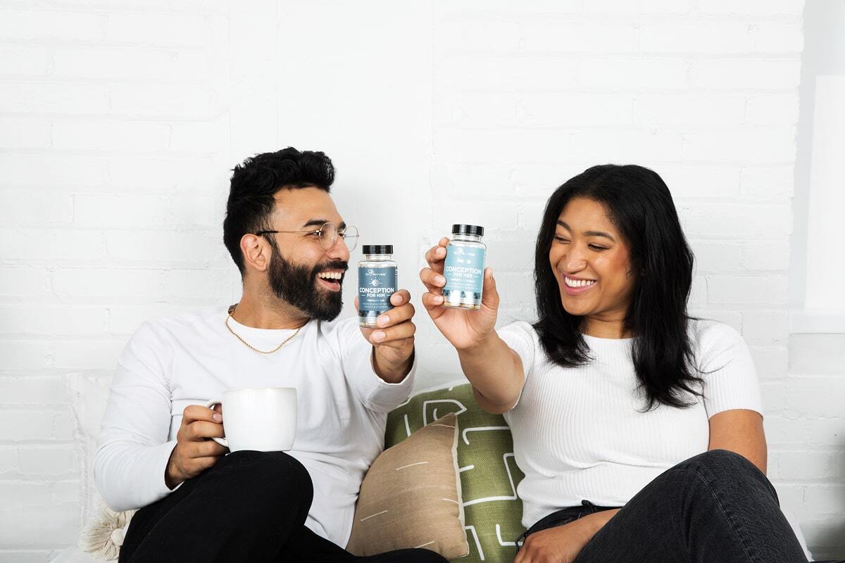Two people smiling, holding supplement bottles, sitting on a couch.