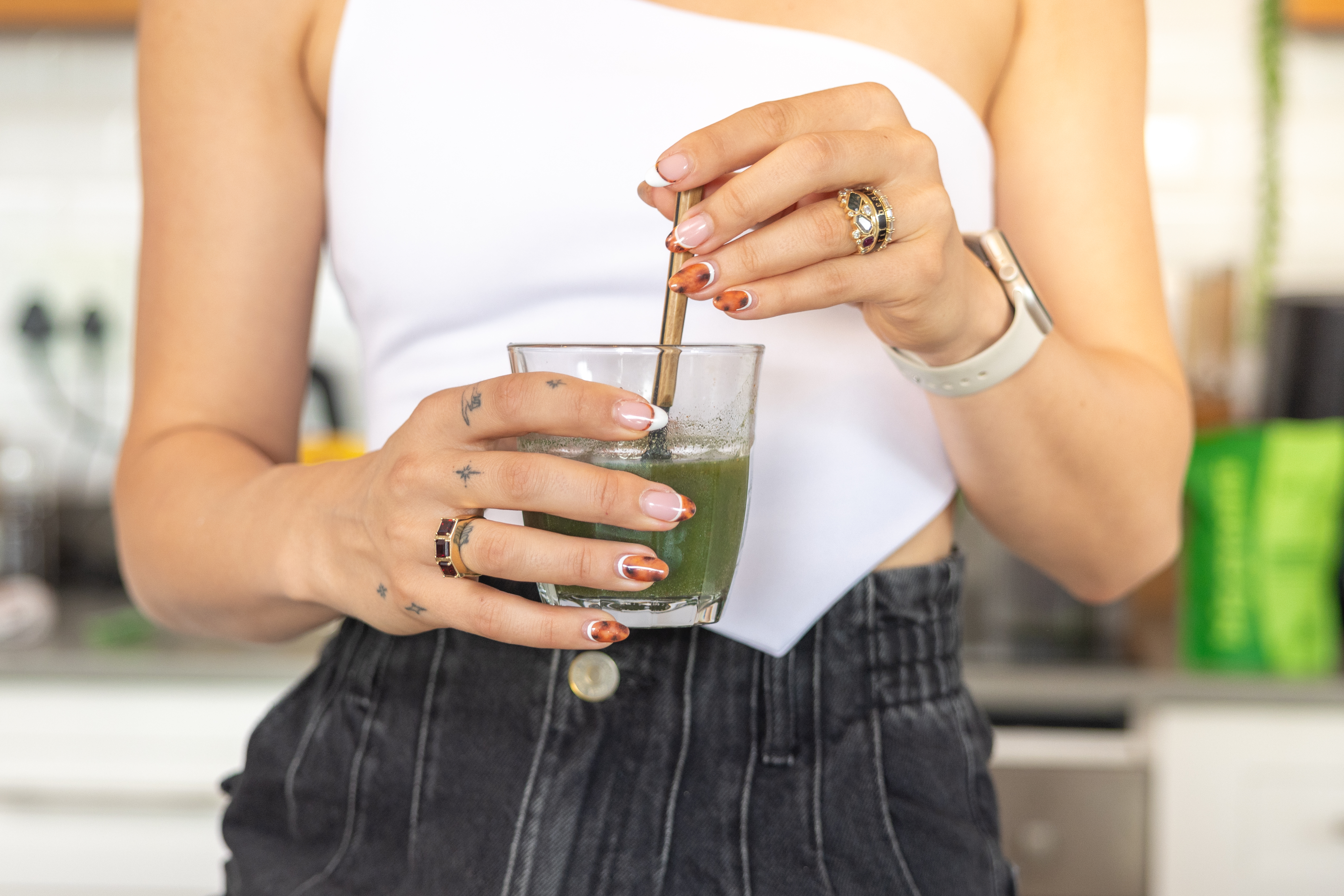 Person stirring a green drink in a glass with a metal straw.