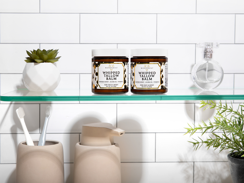 Two jars of whipped tallow balm on a shelf with bathroom items.