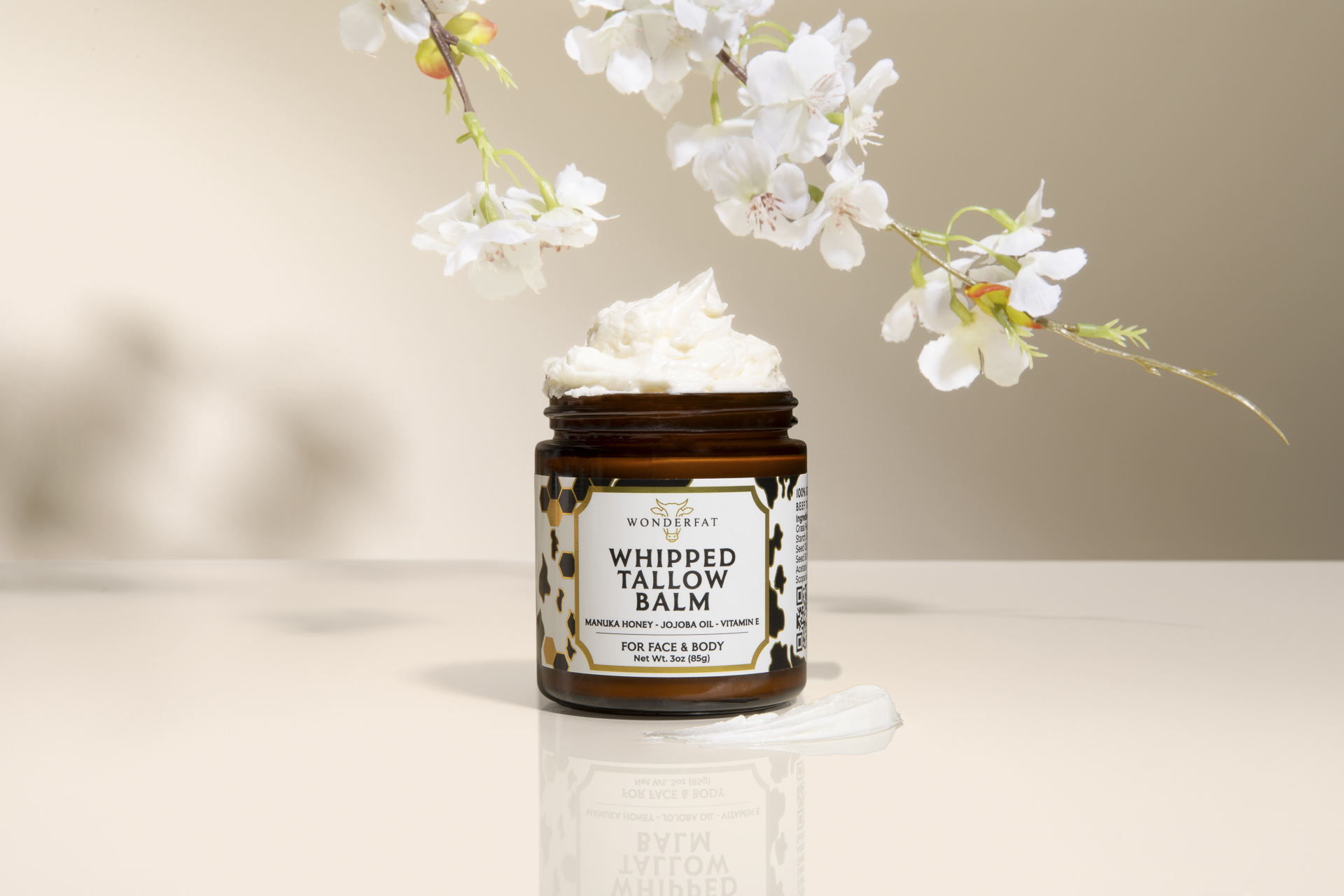 Jar of whipped tallow balm with white flowers above.