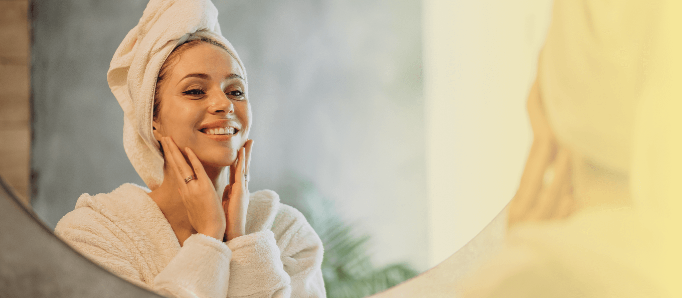 Woman in bathrobe and towel smiling at mirror.