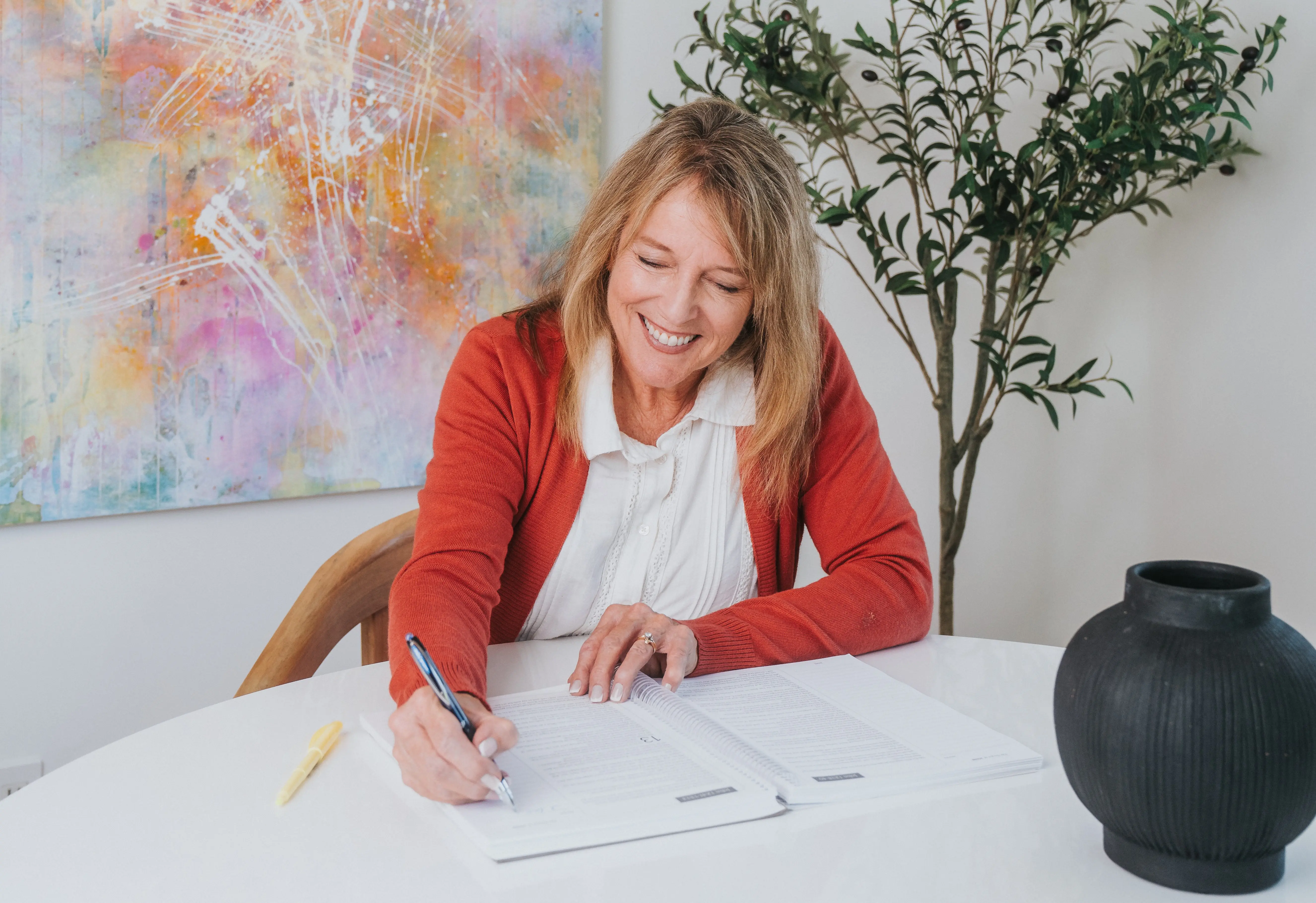 Woman smiling while writing in a notebook at a table.
