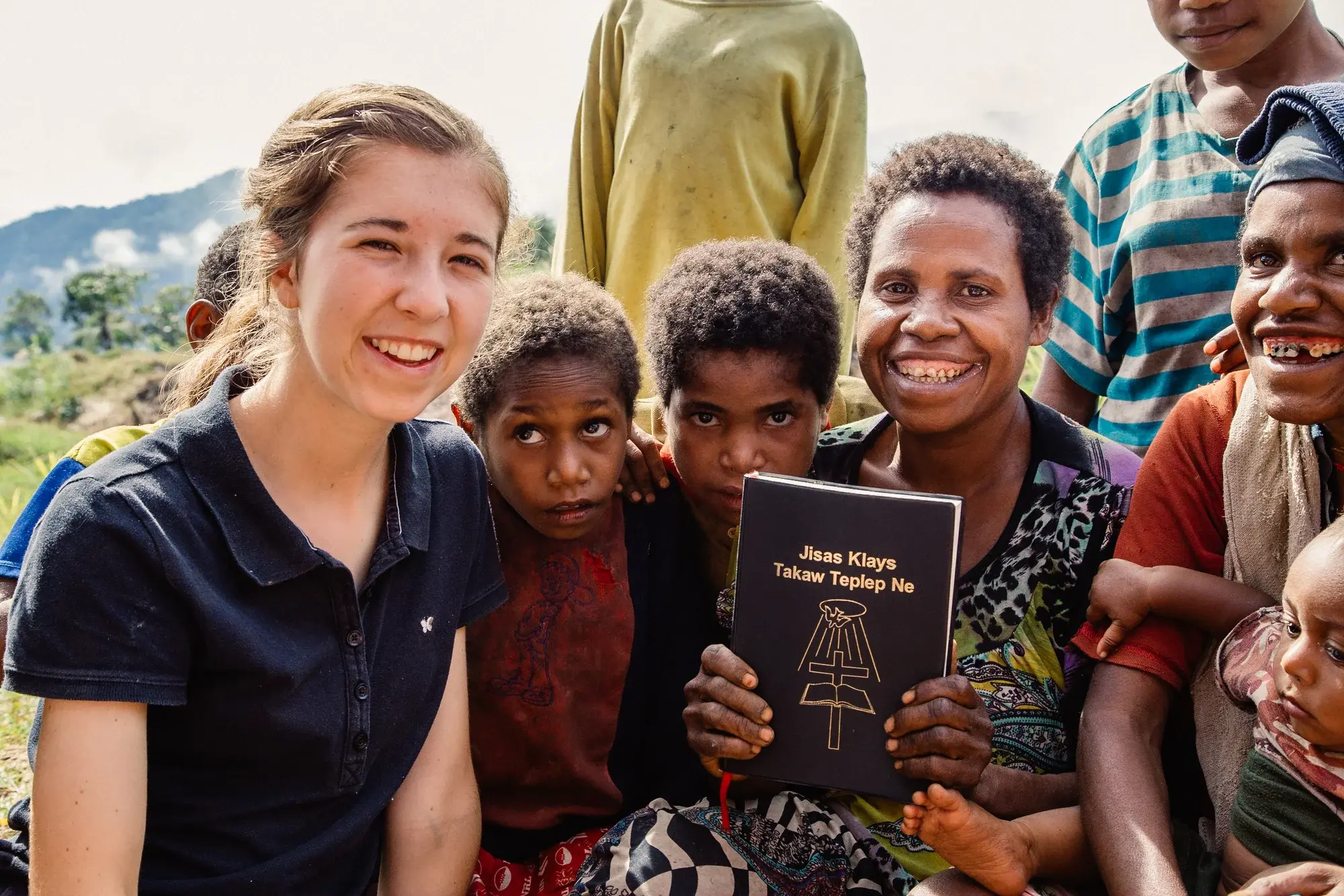 A group of people smiling, holding a book with text.