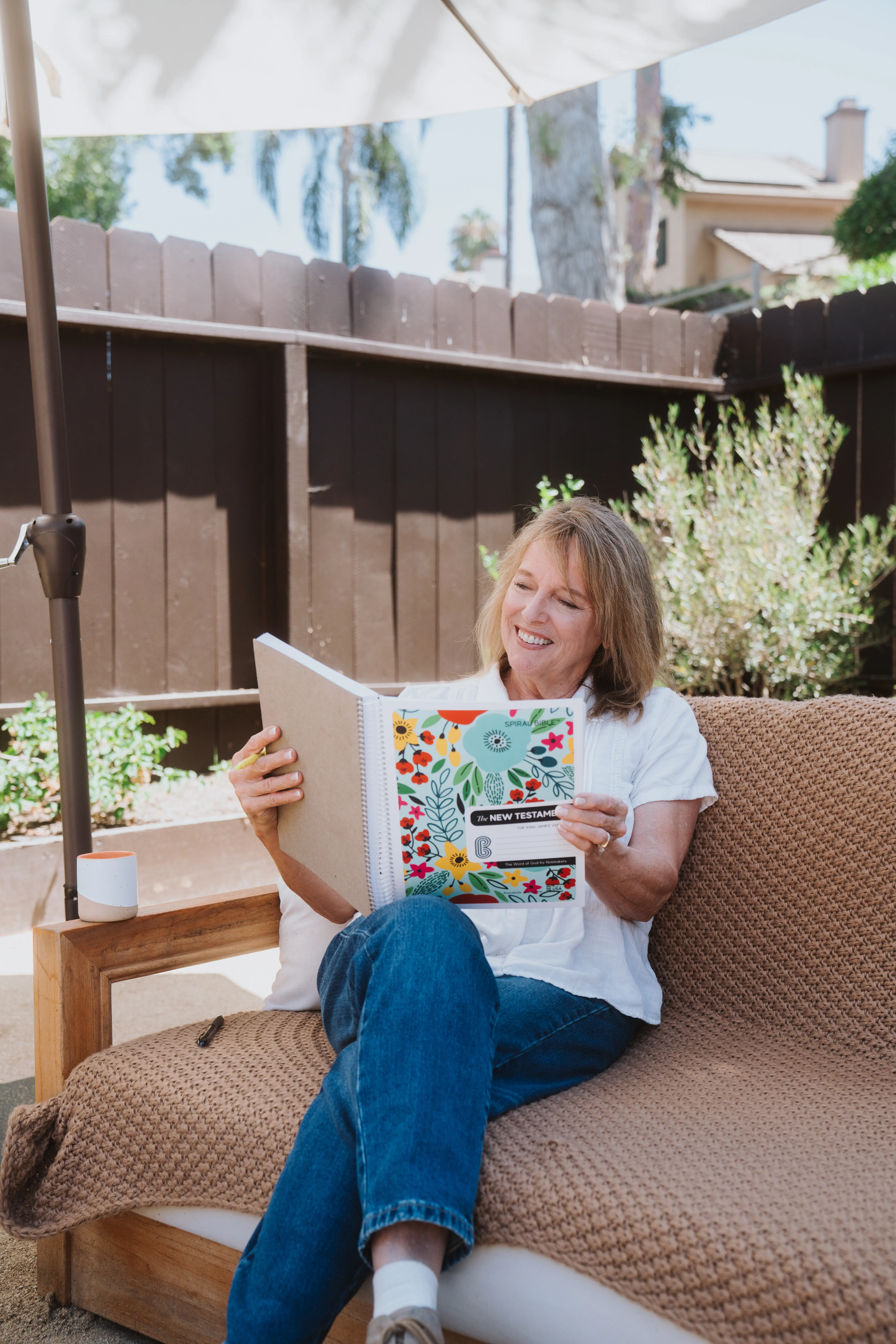 Woman sitting outdoors reading a colorful book on a couch.