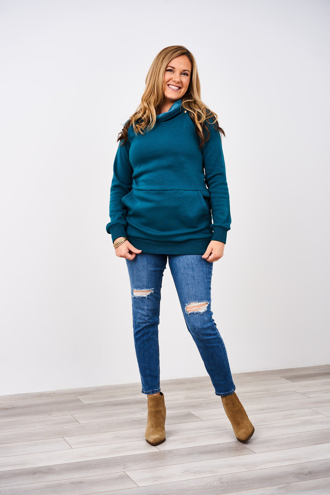 Person in teal hoodie, ripped jeans, and brown boots smiling.