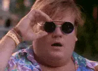 A man with blonde hair and a colorful shirt lowers his round sunglasses, looking surprised.