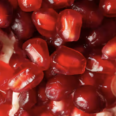 A close-up, macro shot of bright red, juicy pomegranate seeds clustered together.