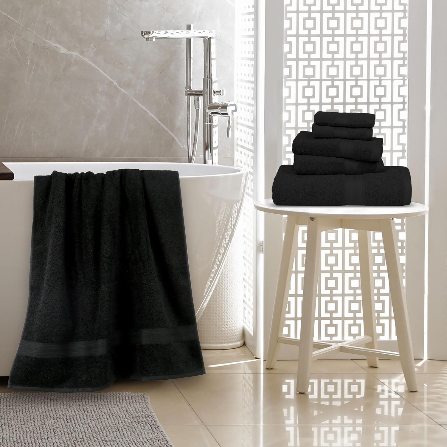 Black towels on a white stool next to a bathtub in a bathroom.