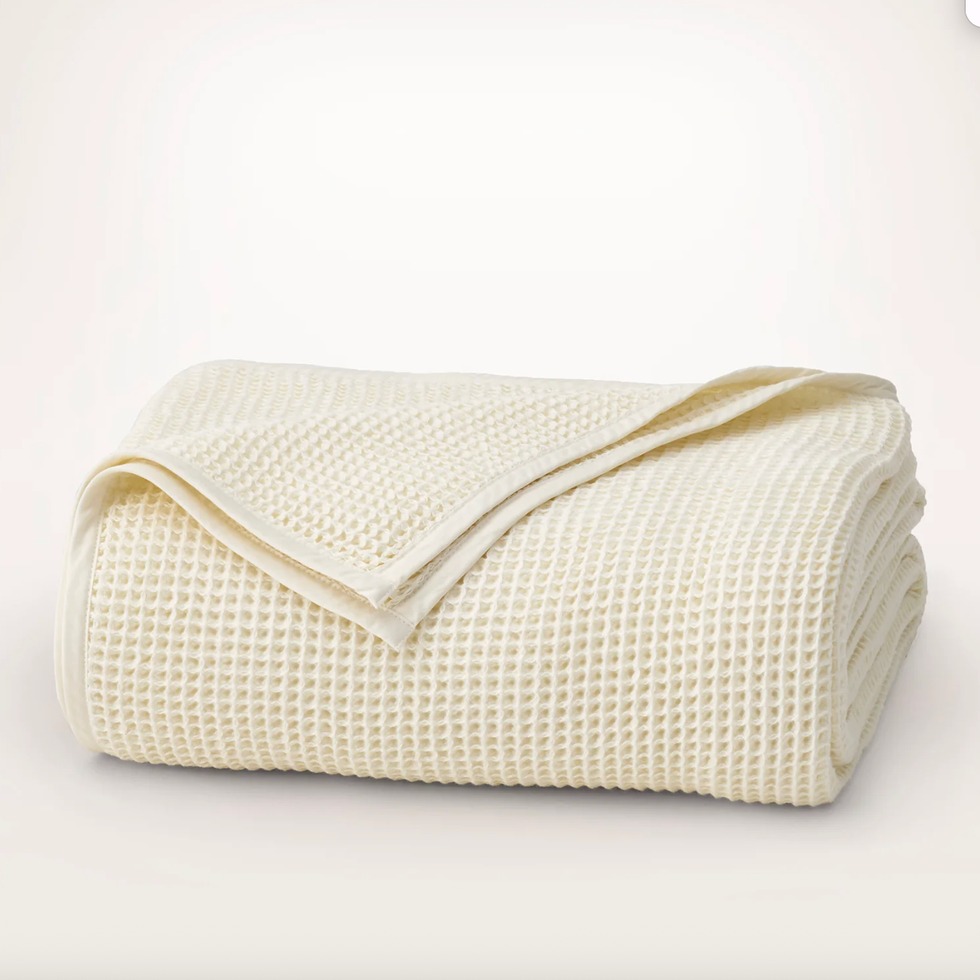 A folded, cream-colored waffle weave blanket on a plain background.