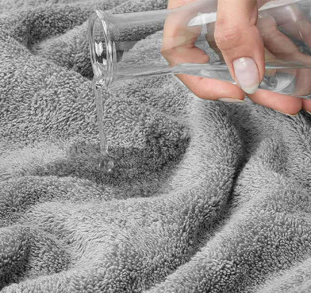 Hand pouring water onto a gray, textured fabric.