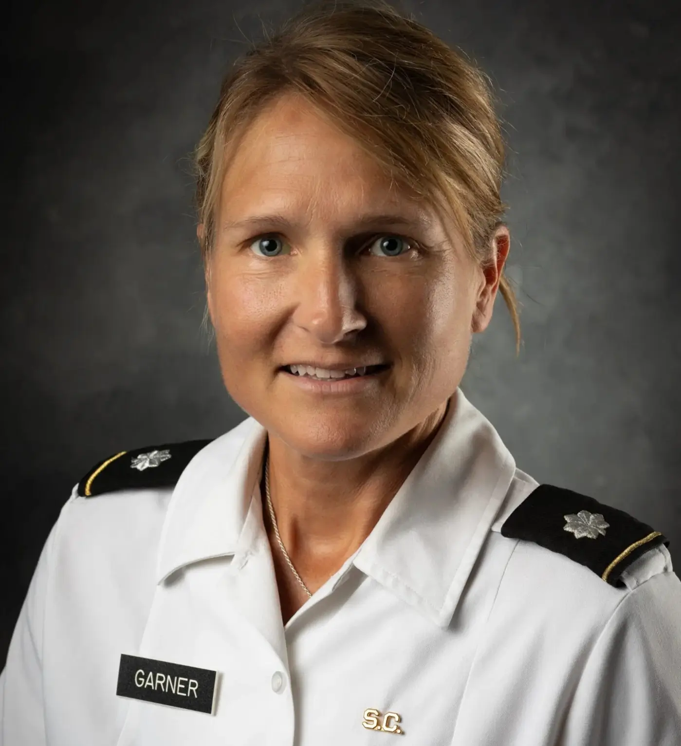 A headshot of a smiling woman with blonde hair in a white military-style uniform with the name tag Garner.