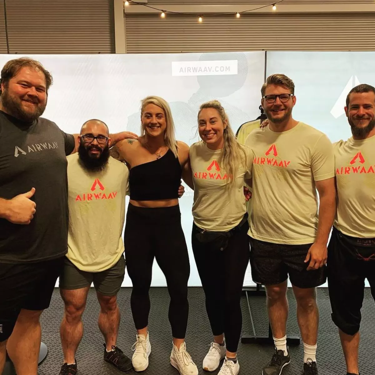 A group of six people wearing AIRWAAV branded t-shirts pose together and smile for a photo.