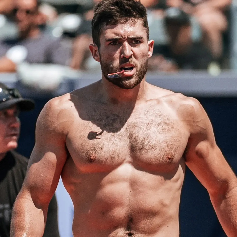A shirtless, athletic man with a beard and a mouthguard has an intense expression.
