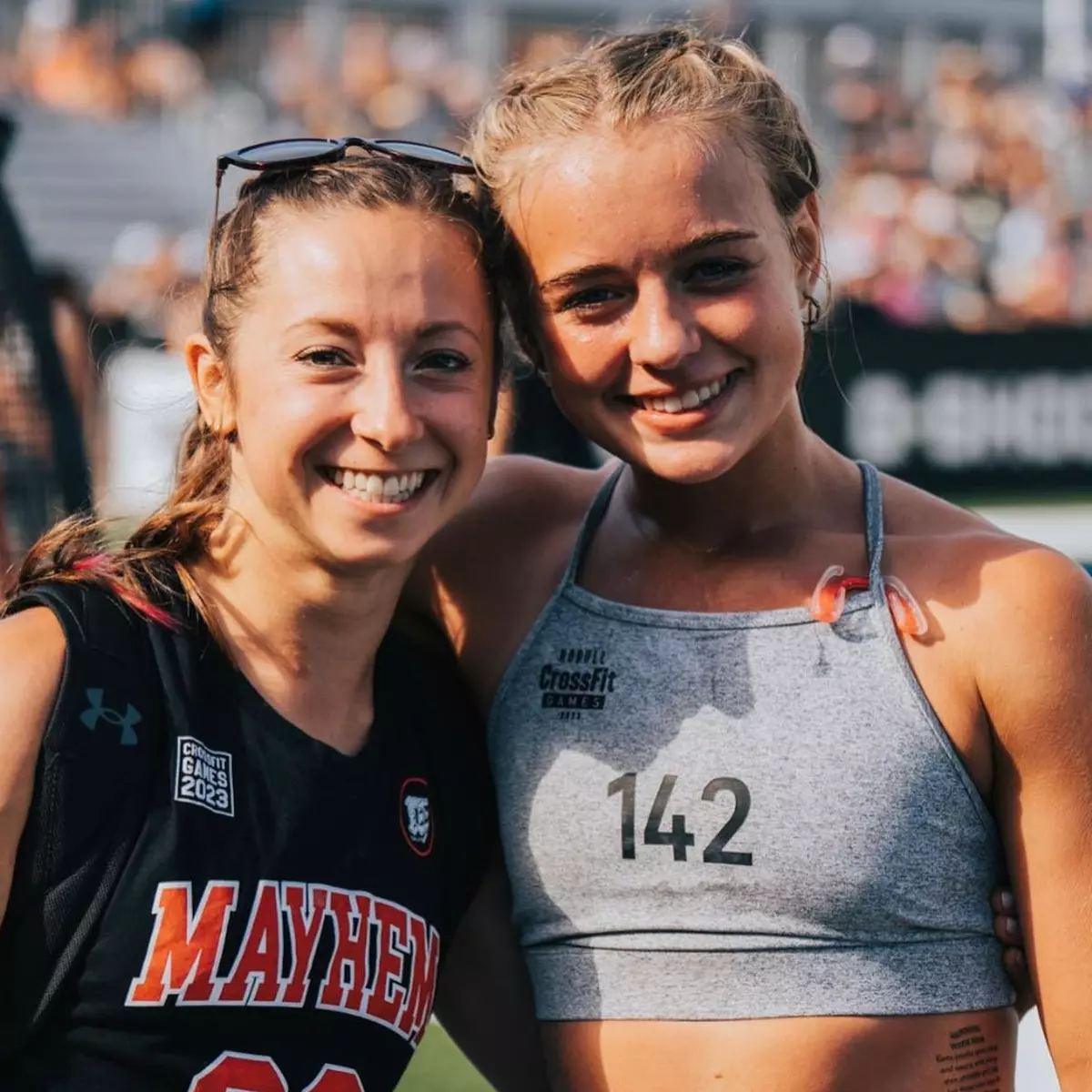 Two female CrossFit athletes smiling and posing for a photo together outdoors.